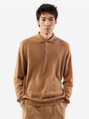 A man standing wearing a beige cashmere polo sweater with a round neckline and long sleeves. #color_light-brown