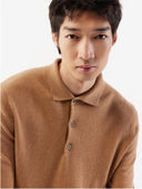 A man standing wearing a beige cashmere polo sweater with a round neckline and long sleeves. #color_light-brown