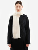 Front view of white lightweight woven scarf draped over a black coat, fringed ends visible