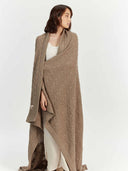 Model wrapped in the full-length taupe throw over a white top, front view