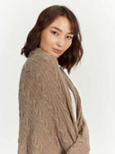 Model draping the taupe cable knit throw over her shoulders, side view
