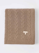 Folded taupe throw laid flat, showing cable panels and ribbed border