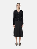 A woman wearing a black lightweight cashmere cardigan with long sleeves and a V-neck collar, paired with a dark skirt.
#color_black