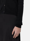 A woman wearing a black lightweight cashmere cardigan with long sleeves and a V-neck collar, paired with a dark skirt.
#color_black